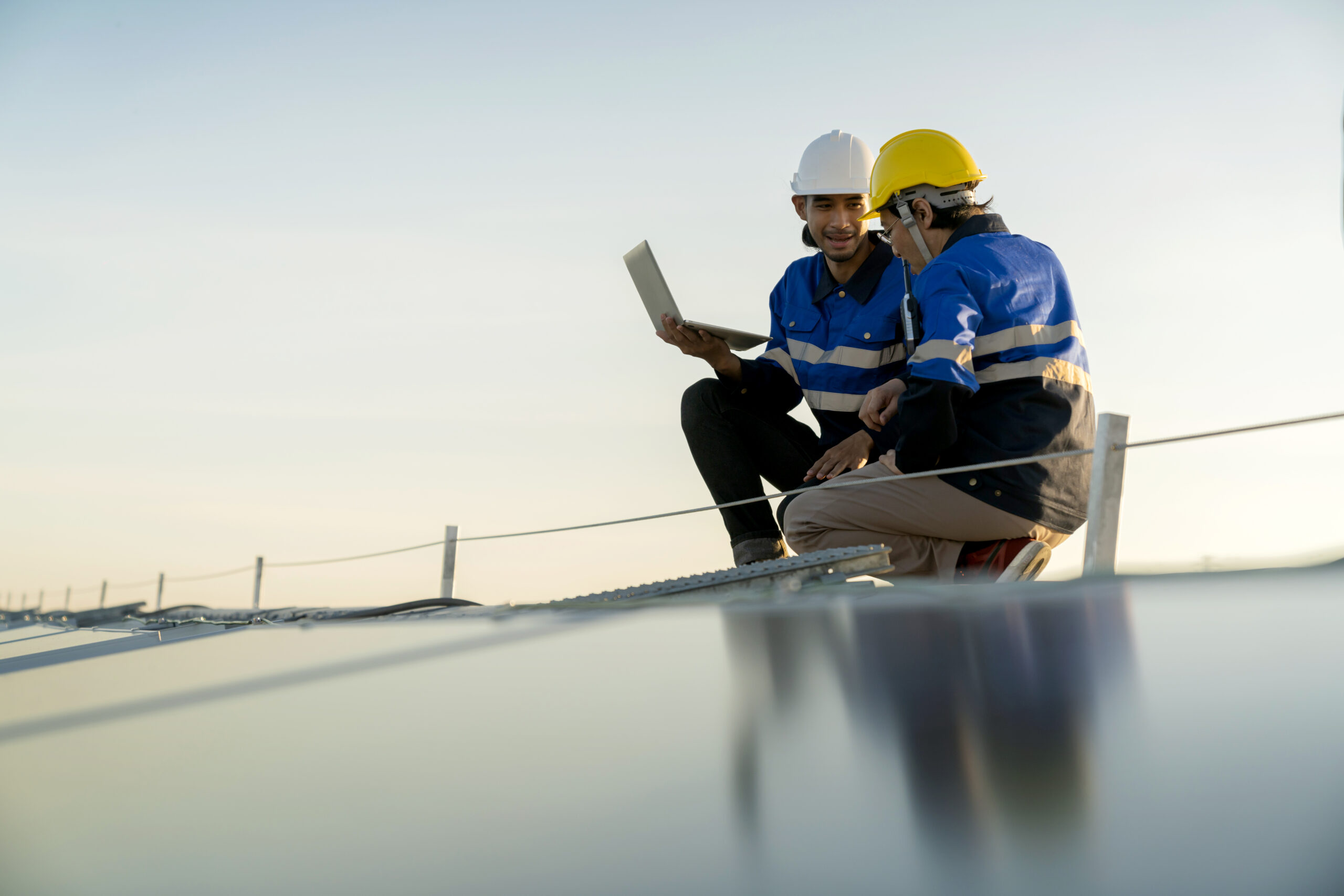 Specialist technician professional engineer with laptop and tablet maintenance checking installing solar roof panel on the factory rooftop under sunlight. Engineers team survey check solar panel roof.